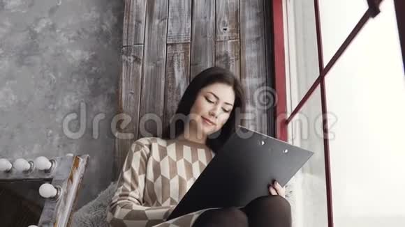 灵感女艺术家穿着靠近窗户的裙子年轻的深色头发的女人坐在窗台上画画视频的预览图
