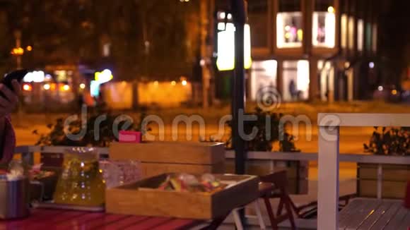 年轻漂亮的红头发女人晚上在马路旁边的街边咖啡馆里用手机晚上很漂亮视频的预览图
