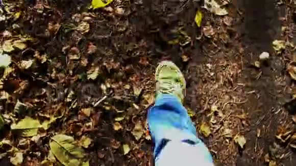 穿着蓝色牛仔裤和绿色运动鞋的脚在秋天的地面上行走视频的预览图