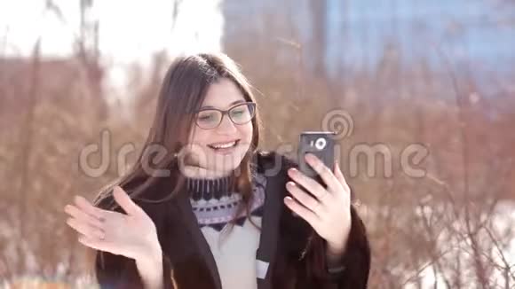 在一个白雪皑皑的冬季城市里一个美丽的女孩在智能手机上使用Skype与家人交流视频的预览图