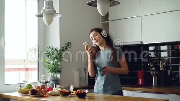 漂亮的快乐女孩在厨房里跳舞唱歌在家里用智能手机听音乐视频的预览图