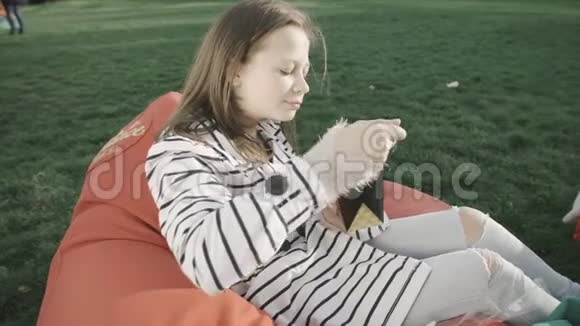 美丽的少女吃着大自然中国面条筷子坐在公园草坪上柔软的红色枕头上视频的预览图