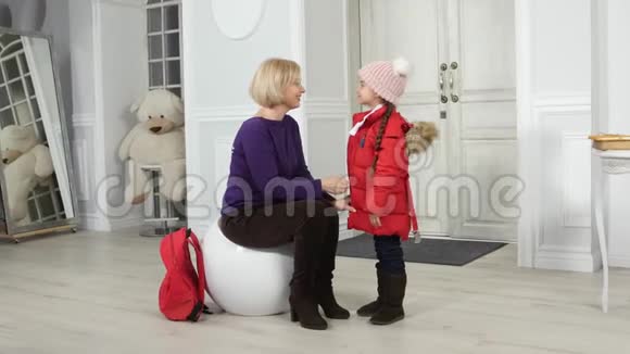 妈妈在走廊里给他的小女儿戴了一件夹克和帽子视频的预览图
