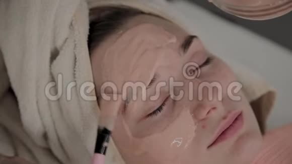 一位专业的美容师用面罩给一个带刷子的年轻女孩美容学的新概念视频的预览图