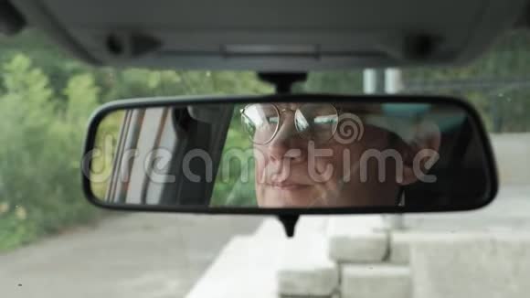 成熟的商人在车里调节眼镜透过镜子观看视频的预览图