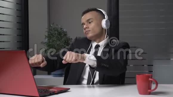 年轻成功的非洲商人西装革履戴着耳机在电脑上听音乐在办公室里跳舞60视频的预览图