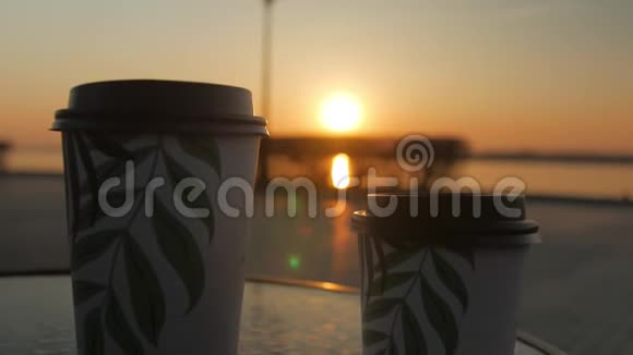 在夕阳的背景下端着咖啡的杯子站在一张桌子上女性手拿着一只视频的预览图