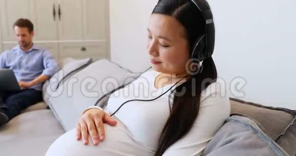 4k客厅的孕妇用耳机听音乐视频的预览图