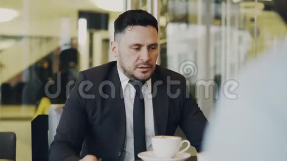 一位留着胡子的白种人商人在玻璃咖啡馆里与投资者做手势讨论他的创业计划视频的预览图