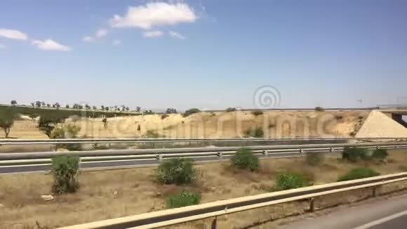 在高速公路上沿着绿树和炎热的沙漠种植汽车可以看到窗外的景色视频的预览图