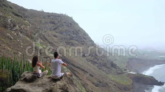 一男一女坐在山顶上看着大海坐在石头上沉思着举起双手视频的预览图