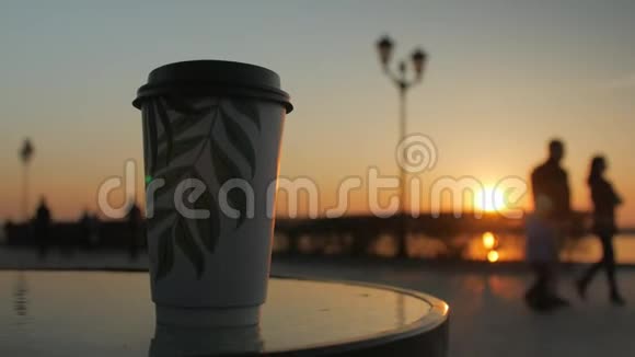 一个咖啡杯站在堤岸背景下的一张街头咖啡馆的桌子上夕阳的天空视频的预览图