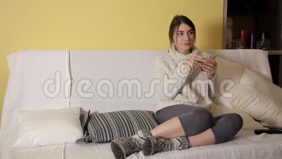 一个年轻的女孩穿着一件舒适温暖的毛衣在冬天的晚上在家喝茶想些什么视频的预览图