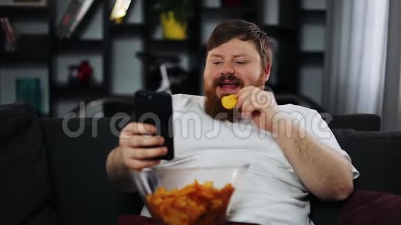 胖子微笑着看着智能手机里的东西吃着薯片视频的预览图