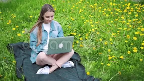 女人坐在公园的绿草上带着笔记本电脑笔记本电脑学生在户外学习视频的预览图