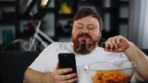 胖子微笑着看着智能手机里的东西吃着薯片视频的预览图