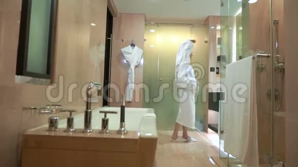 美丽的年轻女子洗完澡后头上戴着毛巾穿着白色外套坐在家里或酒店房间的扶手椅上视频的预览图
