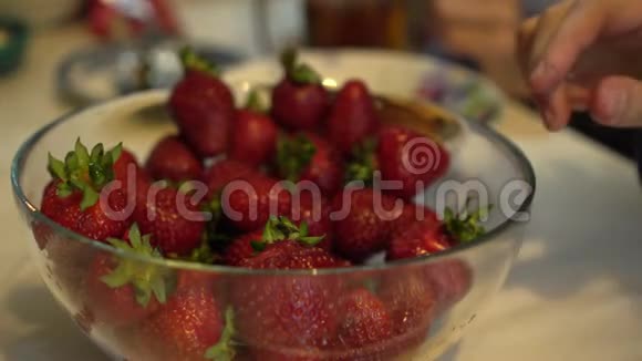 双手试着从玻璃碗里取出新鲜成熟的草莓视频的预览图