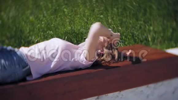 一个美丽的女孩躺在公园的长凳上做着梦享受大自然完成慢镜头回放视频的预览图