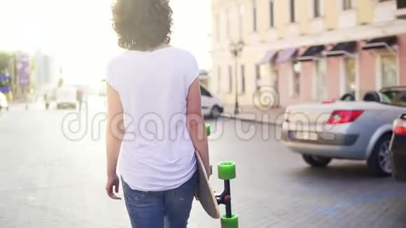 清晨一位女士拿着时髦的长板和鲜花漫步在老城区的街道上视频的预览图