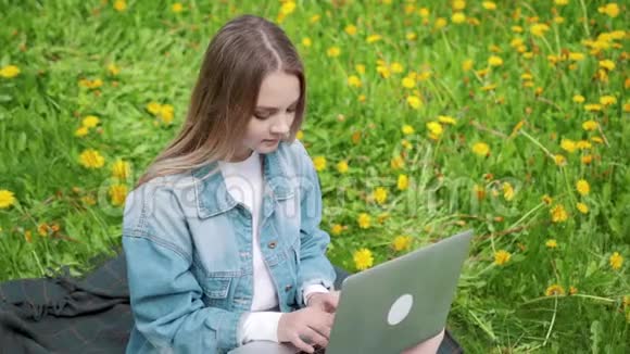 女人坐在公园的绿草上带着笔记本电脑笔记本电脑学生在户外学习视频的预览图