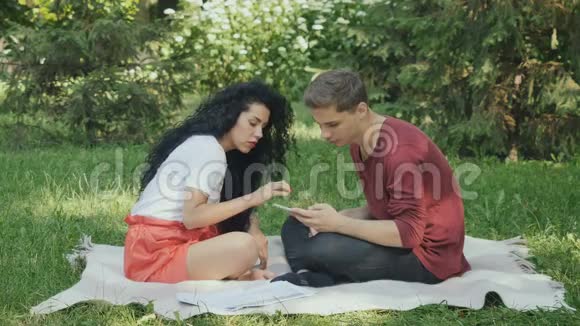 可爱的一对夫妇在格子花格上的公园里使用智能手机视频的预览图
