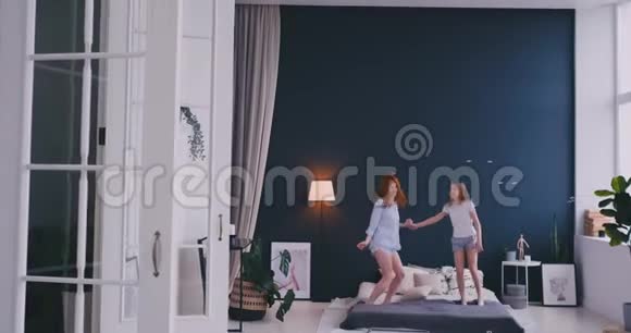 幸福的家庭可爱的女儿和年轻的母亲在床上跳跃和跳舞而在假日的早晨玩得开心视频的预览图