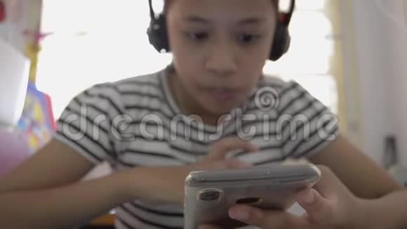 可爱的亚洲女孩看在线视频从智能手机耳机视频的预览图