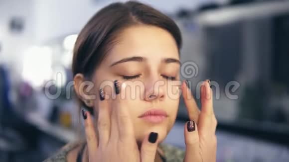 化妆师用她的手在一个年轻女孩的脸上涂上遮瑕膏她也在做按摩完美的基地视频的预览图