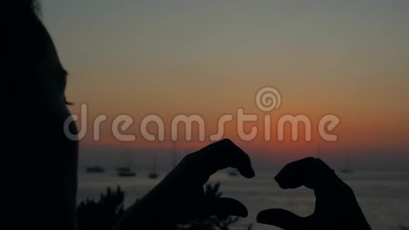 年轻女子在海滩日落时用双手制作心脏标志剪影泰国普吉岛4K视频的预览图