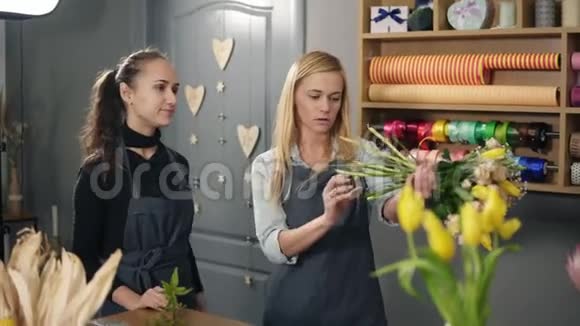 一个金发的花店老板和她的同事围着围裙在花店的柜台前一边数着花束的价格视频的预览图