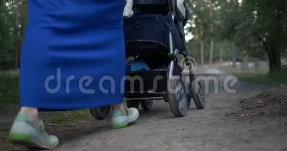 年轻母亲的双腿和蓝色的婴儿车在森林中慢行4k视频的预览图