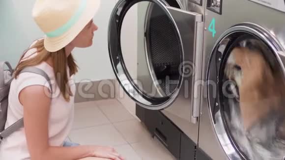 洗衣机房戴帽子的年轻女子看洗衣店洗衣服专注于洗衣机视频的预览图
