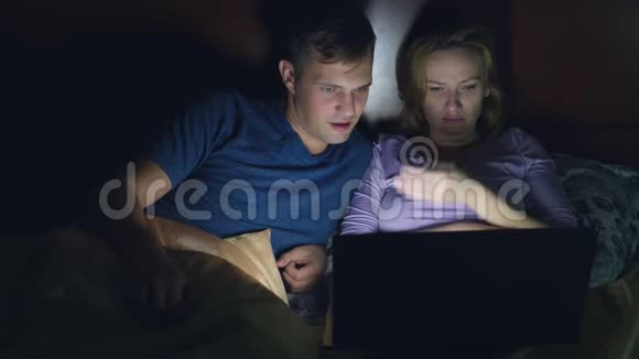 夫妻男人和女人在睡觉前在卧室的床上用笔记本电脑看电影看恐怖电影观众视频的预览图