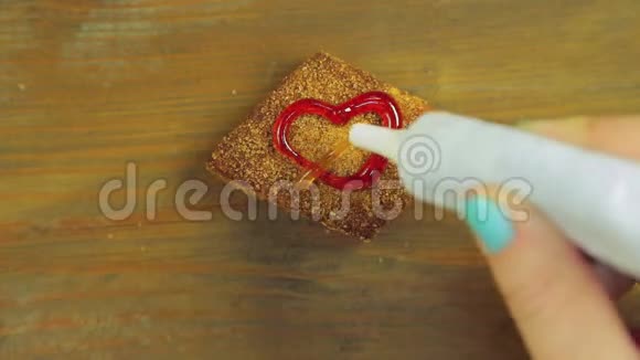 一只手握着一管烹饪颜料在一块带有红色颜料的巧克力饼干上画着心手工制作视频的预览图