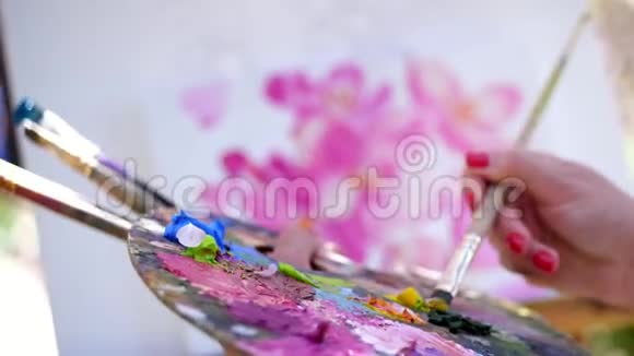 特写镜头女性的手画家艺术家画一幅花的画她拿着颜料和画笔的调色板混合视频的预览图