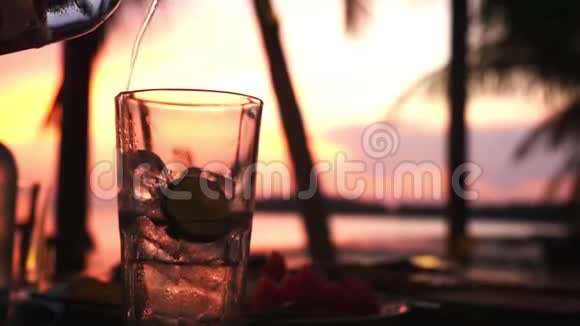 在一家海滩咖啡馆里矿泉水正倒在玻璃上背景是夕阳下的冰慢动作1920x1080个视频的预览图