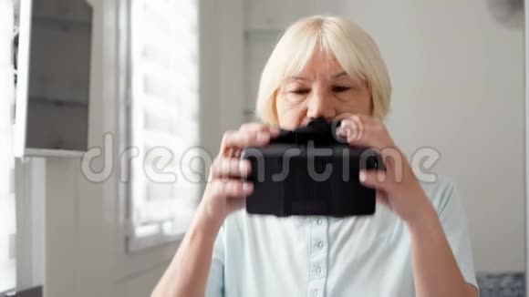 漂亮的金发白衣老太太在家里用VR360眼镜活跃的现代老年人视频的预览图