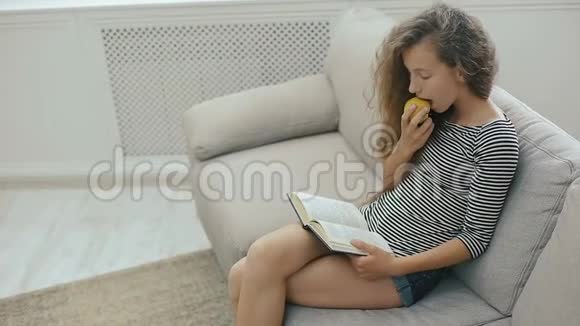 美丽的少女在沙发上放松看书吃苹果视频的预览图
