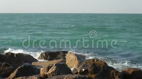 在阳光明媚的日子里美丽多彩的海浪在防波堤上冲刷着大石头视频的预览图
