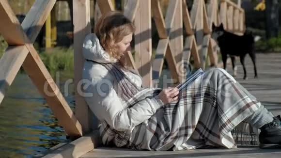 秋河附近的桥上一个女人正在看书一只黑狗正在附近散步视频的预览图