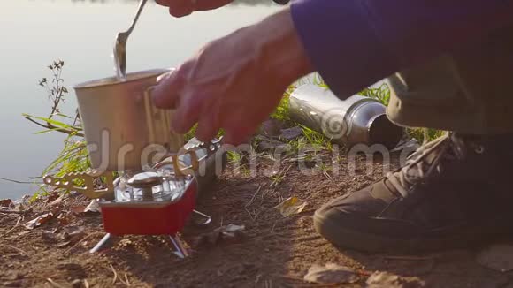 在湖边的秋天森林里男人的手在煤气炉上做食物或热饮视频的预览图