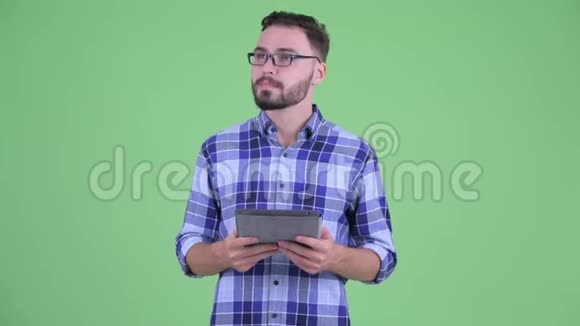 快乐的年轻有胡子的嬉皮士在使用数码平板电脑时思考视频的预览图