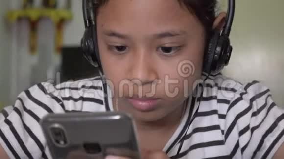 可爱的亚洲女孩看在线视频从智能手机耳机视频的预览图