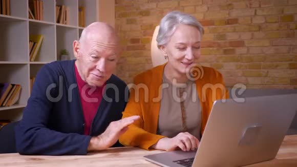 两位头发花白的高加西亚同事在笔记本电脑上用视频聊天在办公室里很开心视频的预览图