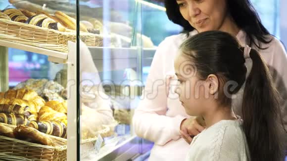 可爱的小女孩在橱窗里挑选糕点和她妈妈一起购物视频的预览图