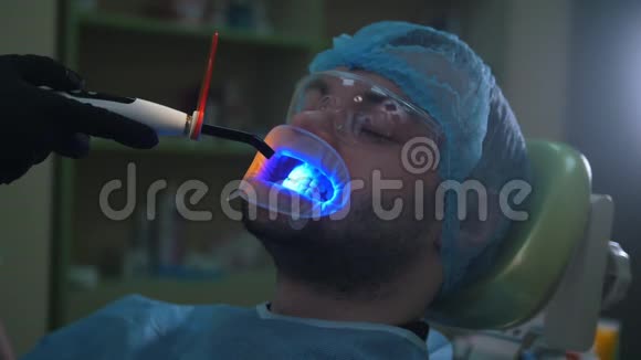 医生和病人在牙科办公室用扩唇器用紫外线和橙色保护屏清洁视频的预览图