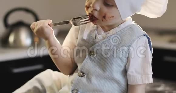 一个戴着烹饪帽的脏男孩在厨房里用叉子吃巧克力视频的预览图
