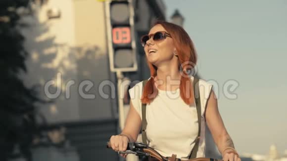 骑着自行车站在红绿灯背景上的红发女子肖像视频的预览图