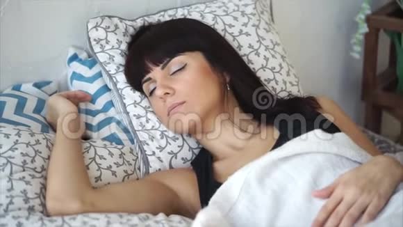 年轻漂亮的黑发女人正在阳光明媚的早晨睡在床上特写镜头视频的预览图